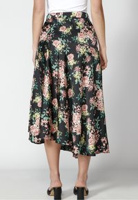 Kukallinen hame mustalla pohjalla, jossa on vaaleanpunaisia ja vihreitä kukkia. Kangas näyttää silkkiseltä, jossa on liehuva muoto ja joustava vyötärönauha.