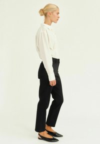 Biela košeľa s button-up, čierne prispôsobené nohavice a čierne špicaté balerínky. Hladká tkanina, štruktúrovaný dizajn a priliehavá silueta. Minimalistický štýl.