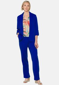 Kuninglik sinine bleiser ja pükste komplekt mustrilise pluusiga, millel on erksad lehekujundid. Sile kangas ja kohandatud lõige, koos hõbedaste kontsadega.