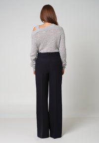Grijze, oversized gebreide trui met open schouderontwerp, gecombineerd met hoge zwarte wijde broek. Zachte textuur, minimale details.
