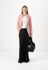 Blazer en velours côtelé rose clair, top blanc à côtes, pantalons noirs à jambes larges et sac à main rond noir. Textures lisses et coupe ajustée.