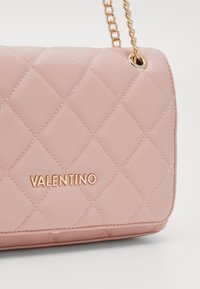 Pink quilted bag with gold chain strap, featuring stitched diamond pattern and gold "Valentino" logo on the front.