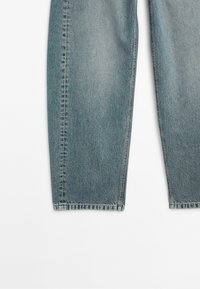 Světlé modré džíny s rovný střih, viditelným šitím a roztrhaným lemem na spodní straně. Tkanina má mírně opotřebovaný vzhled.