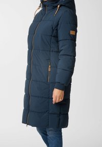 Manteau rembourré navy avec une capuche, présentant des sections à motif matelassé horizontal, une fermeture éclair avant et des accents beige sur la fermeture éclair et les manches.