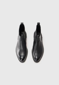 Botas chelsea de cuero negro con textura suave, puntera afilada y paneles laterales elásticos. Presentan tiradores para facilitar su uso.