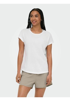 Woman with long braided hair wearing a white short-sleeve t-shirt and light beige shorts, smiling and looking to the side.