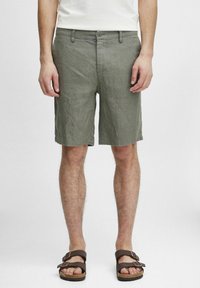 Lys grå linstoffshorts med flat front, sidelommer og knappelinning, kombinert med brune sandaler på barføtt.