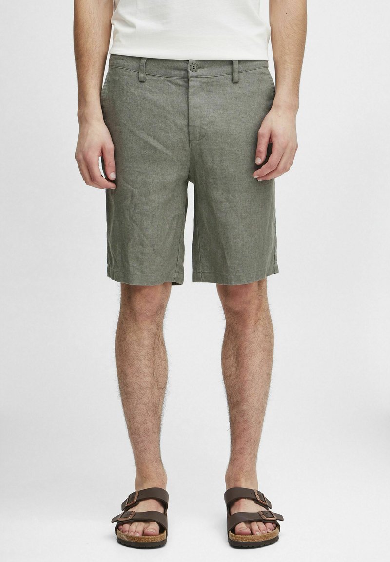 Lys grå linstoffshorts med flat front, sidelommer og knappelinning, kombinert med brune sandaler på barføtt.