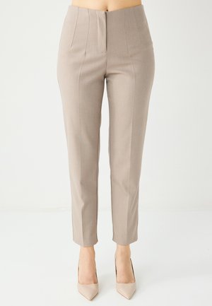 Pantaloni beige su misura con taglio dritto, pieghe frontali e lunghezza alla caviglia; abbinati a scarpe con tacco nude.