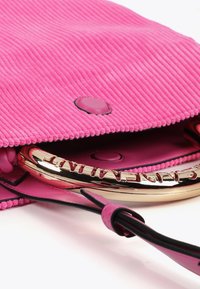 Borsa in corduroy rosa brillante parzialmente aperta, che rivela un manico dorato lucido e un interno rosa, mettendo in mostra texture morbide e colori vivaci.