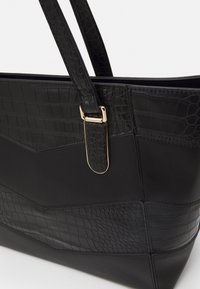 Sac fourre-tout noir en cuir lisse et texturé, avec des accents imitation crocodile, une boucle en métal doré et un design structuré.