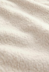 Țesătură dintr-o fleece de culoare crem, cu o suprafață texturată și pufoasă. Materialul prezintă valuri fine și delicate, având un aspect ușor.