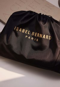 Zwarte satijnen trekkoordzak met in goud geperst tekst "ISABEL BERNARD PARIS". Gladde textuur, gathered top, slank ontwerp.