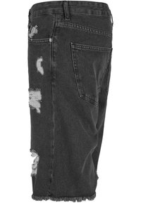 Shorts de mezclilla negra con un diseño desgastado, que presentan múltiples desgarros y dobladillos deshilachados. Estilo clásico de cinco bolsillos y presillas para cinturón.