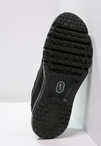 Sole di scarpa sportiva nera con texture in gomma antiscivolo, lieve curvatura al tallone e logo visibile al centro.