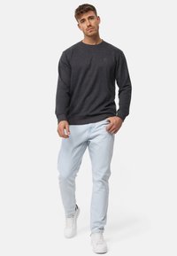 Sudadera gris oscuro en mezcla de algodón, de mangas largas, cuello redondo, con puños acanalados, combinada con jeans azul claro y zapatillas blancas.