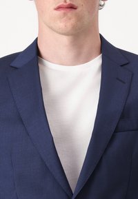 Dunkelblaues Blazer aus strukturierter Stoff, mit Reverskragen und einer Brusttasche, kombiniert mit einem weißen Rundhalsausschnitt-T-Shirt.