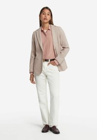 Blazer i strukturerad ljusbeige, med slagkrage över en rosa blus, kombinerad med vita jeans och vinröda loafers.