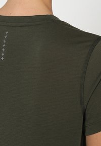 Mörkgrön kortärmad skjorta med en jämn textur, som har ett subtilt mönster av små grå kors längs den centrala bak sömmen.