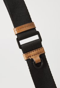 Cintura nera in nylon con finitura texturizzata, dotata di un accento in pelle marrone e hardware nero, progettata per una lunghezza regolabile e una durata elevata.