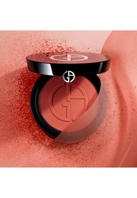 Blush crème rouge dans un compact noir brillant avec un couvercle logotypé, affichant une texture lisse et une finition douce et naturelle.