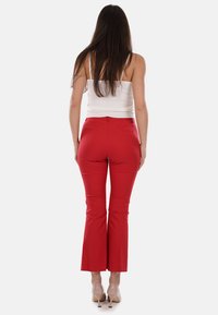 Pantaloni rossi a campana realizzati in tessuto elasticizzato con una trama liscia, con vita medio alta e tasche posteriori, abbinati a una maglietta bianca.