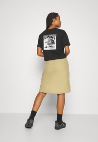 T-shirt preto de manga curta com uma impressão gráfica branca nas costas, combinado com uma saia bege e calçado preto. A textura parece suave.