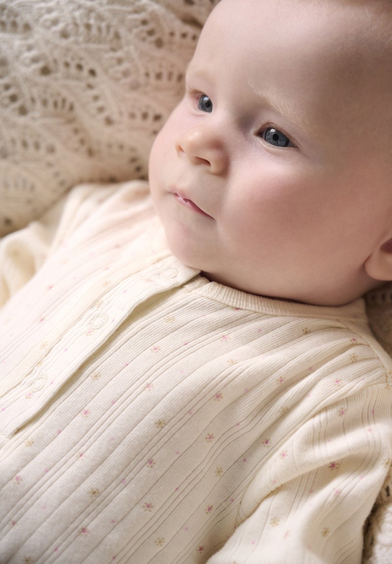 Body côtelé beige clair avec petits motifs floraux roses et dorés, col rond et boutons à l'avant.