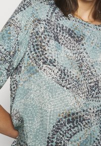 Top corto a maniche corte blu con motivo astratto nelle tonalità della navy, bianco e oro, caratterizzato da un tessuto testurizzato e una vestibilità morbida.