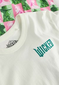 Vit bomull t-shirt med grön broderad "WICKED"-logotyp. Tyget är mjukt, med en ribbad hals och ett färgglatt mönstertryck på baksidan.