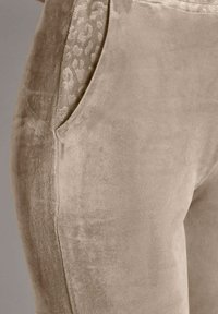 Beige velours leggings met een gladde textuur, voorzien van een subtiele dierenprintaccent op de zijzakken. Inclusief elastische tailleband.