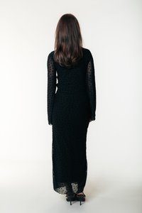 Svart klänning med långa ärmar i genomskinligt prickigt tyg, figurnära siluett och golvlång design. Bärs med svarta högklackade skor.