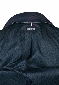 De binnenkant van de Hechter Paris-jacket heeft een donkere, gestreepte voering met een geometrisch ontwerp. Bevat een label met de merknaam en een rode accent.
