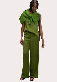 Grøn ribbet top med korte ærmer, kombineret med løse grønne bukser med vidde i benene. En matchende grøn sweater er lagt over skuldrene.