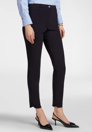 Pantaloni slim-fit navy con una texture liscia, caratterizzati da una chiusura con bottone e dettagli sottili all'orlo. Abbinati a tacchi neri a punta.
