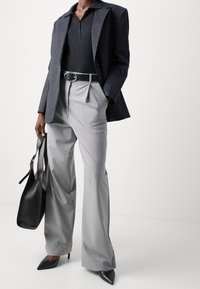 Skräddarsydd svart kavaj med ränder, åtsittande svart polo, ljusgrå hög midja byxor, svart bälte, spetsiga svarta klackar och en svart handväska.