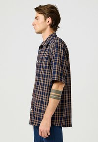 Korte mouwen geruite blouse in marineblauw en bruin, met een button-down kraag, een borstzak en een lichte stof met een gestructureerd patroon.