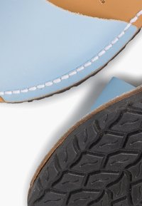 Světle modrá kožená sandál s prošívaným okrajem, hnědou stélkou a černou texturovanou gumovou podrážkou s vzorovaným gripem.