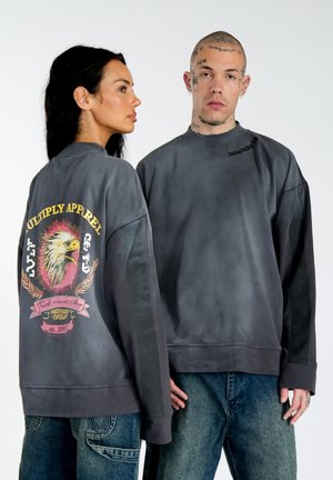 Oversized gray sweatshirt featuring a graphic of an eagle, colorful banner, and "Multiply Apparel" text on the back. Soft texture.