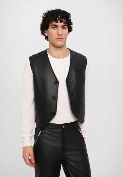 Gilet en cuir noir avec fermeture à boutons, disposant d'une poche poitrine unique et d'une texture lisse, porté sur un haut à manches longues blanc.