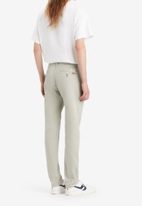 Jasnoszare bawełniane spodnie o prostym kroju, z tylnymi kieszeniami, subtelnymi detalami szwów, noszone z białymi butami z ciemnoniebieskimi akcentami.