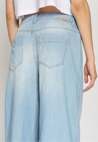 Ljusblå denimjeans med en avslappnad passform, som har två bakfickor och subtila blekningar på tyget, vilket ger en slät yta.