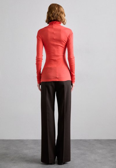 Long-sleeve turtleneck in coral fabric, fitted design. Paired with wide-leg dark brown trousers, both showing smooth textures and tailored fit.
