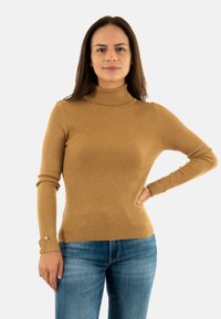 Maglione a collo alto a coste in marrone chiaro, design aderente con maniche lunghe e dettagli con bottoni ai polsini, abbinato a jeans blu.