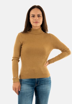 Pull à col roulé côtelé de couleur marron clair, design ajusté avec des manches longues et détails de boutons aux poignets, associé à un jean bleu.