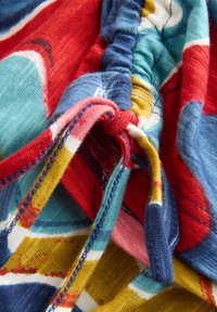 Tessuto multicolore con motivi astratti in rosso, blu, turchese, giallo e rosa. Texture arricciata con chiusure legate.