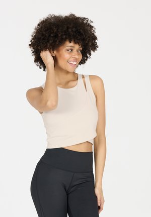 Hellbeige, kurzes Tanktop mit asymmetrischem Design und dünnen Trägern, kombiniert mit hochgeschnittenen schwarzen Leggings. Glatte Stoffoberfläche.