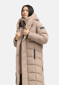 Gestepte lange jas in zacht beige, met hoge kraag, zwarte ritszakken en een gewatteerde textuur. Voorzien van een opvallende capuchon en merkdetail.
