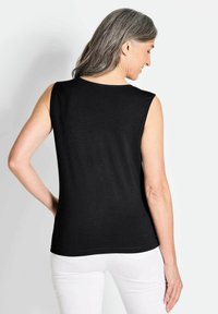 Schwarzes ärmelloses Top mit glatter Textur und Rundhalsausschnitt, verfügt über eine taillierte Silhouette; getragen mit weißen Hosen. Rückansicht angezeigt.