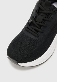Black athletic shoe featuring a knitted upper, textured pattern, black laces, and a white midsole with a durable rubber outsole.
